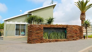 A modern building with a sloped roof, a glass entrance, and a stone wall with plants.