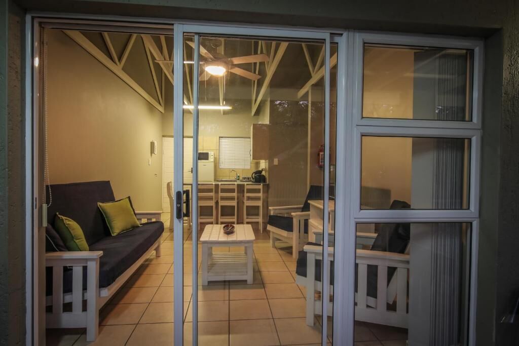 A room with a sofa, a small table, and a chair, with a sliding glass door leading to a kitchen area.