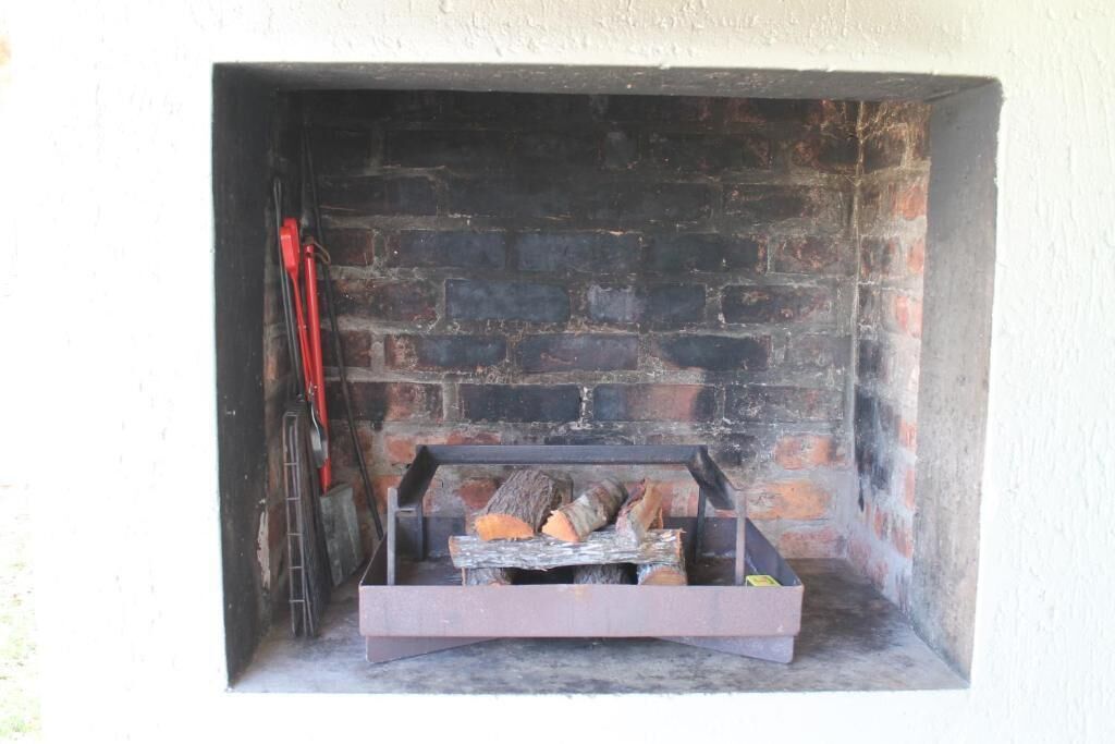 A fireplace with a metal grate, a brick wall, and a ladder leaning against the wall.
