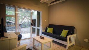 A living room with a sofa, a coffee table, a TV, and a sliding glass door leading to an outdoor area.