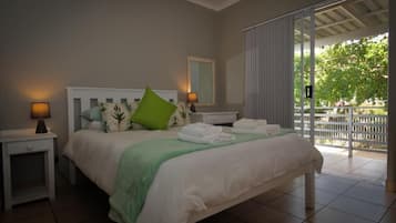 A bedroom with a bed, nightstands, a mirror, and a sliding glass door leading to an outdoor area.