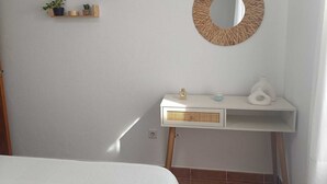 Um quarto com cama, mesa de cabeceira branca com abajur, espelho e prateleiras fixadas na parede com objetos decorativos.