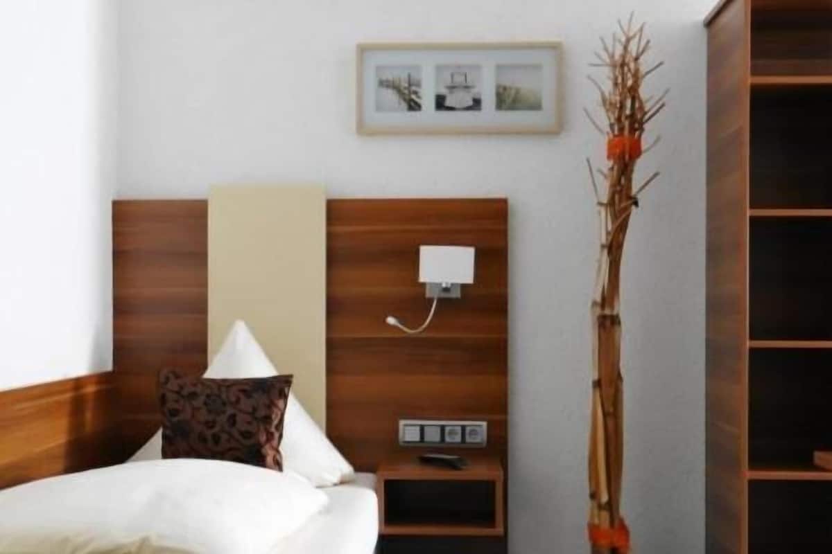 A hotel room with a bed, bedside table, lamp, wall-mounted phone, and a decorative plant.