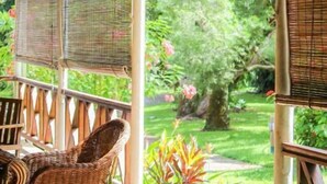 A covered outdoor seating area with wicker furniture and a view of a garden.