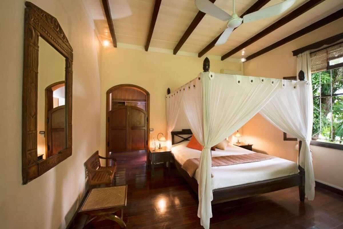 A four-poster bed with a canopy, a wooden desk with a chair, a large mirror, and a door.