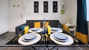 Ein Esstisch mit Geschirr, Besteck und Gläsern, ein Sofa mit Kissen, eine an der Wand befestigte Elektroinstallation und eine Tür mit Hinweisschildern.