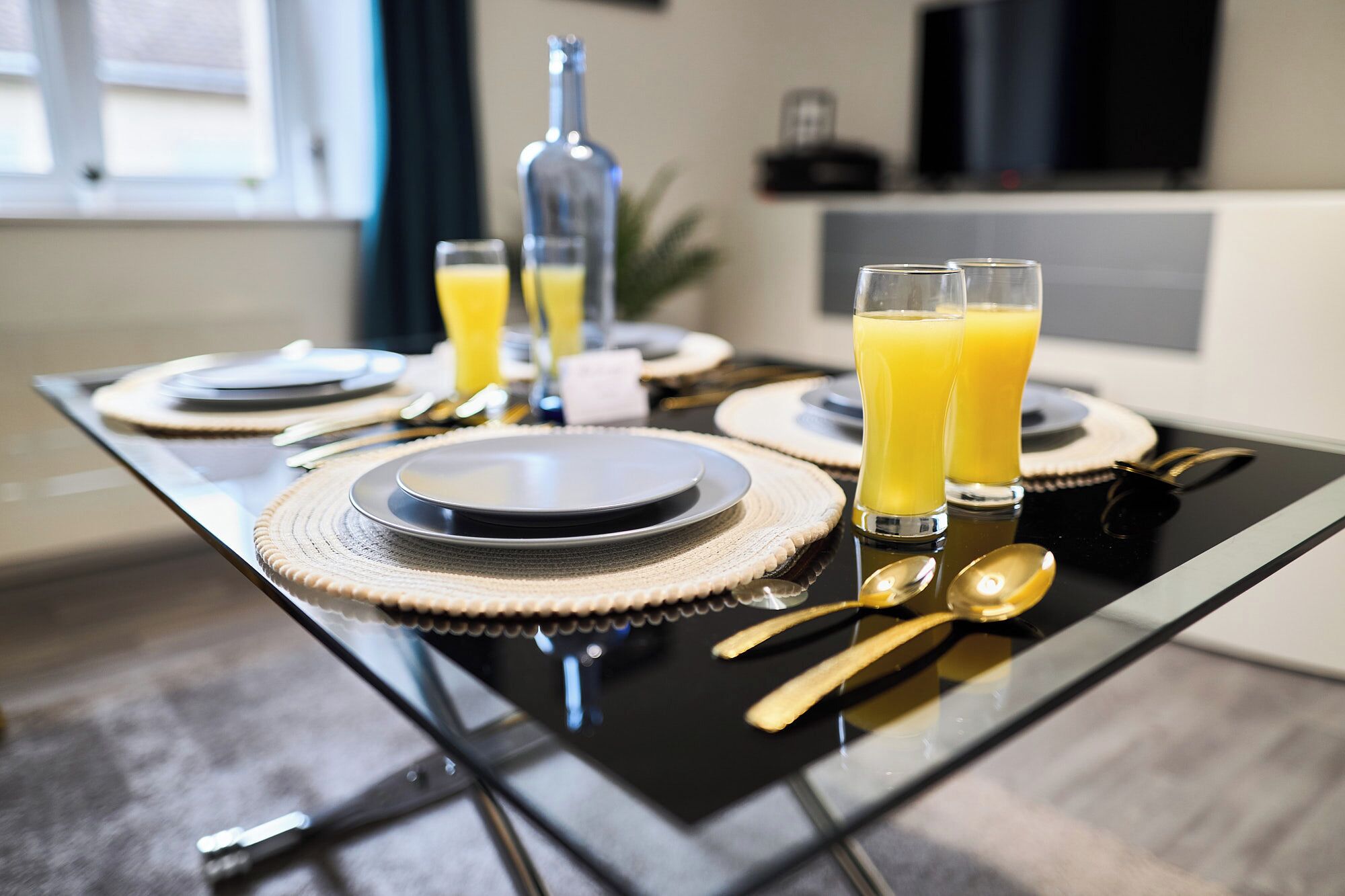 A dining table set with plates, cutlery, and glasses of orange juice.