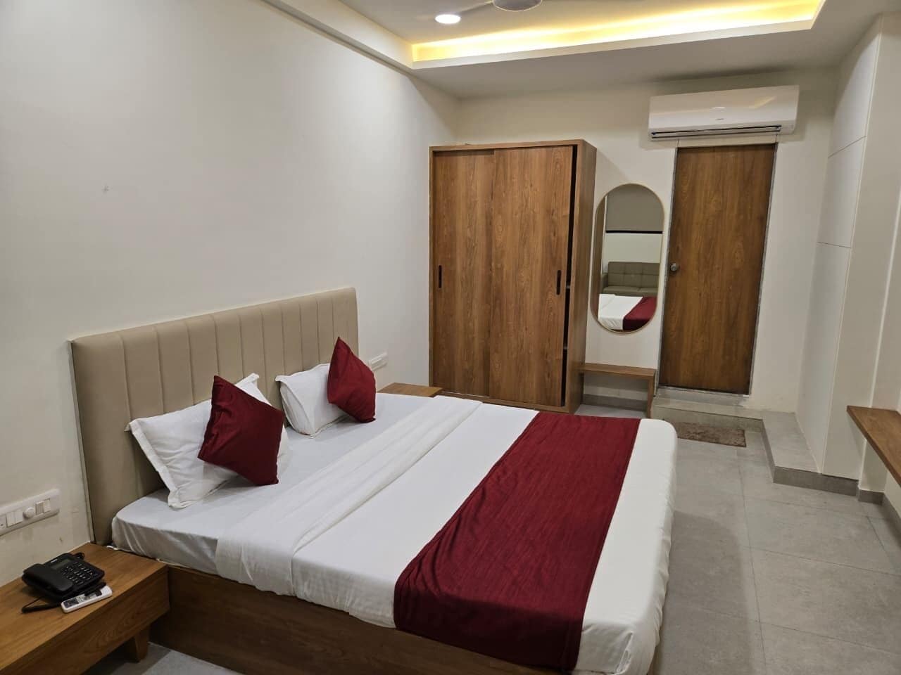A hotel room with a bed, a wardrobe, a mirror, and an air conditioning unit.