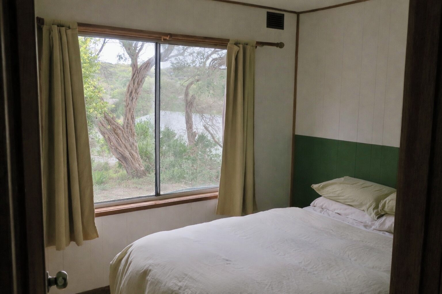 Een kamer met een bed, een raam met gordijnen en uitzicht op bomen.