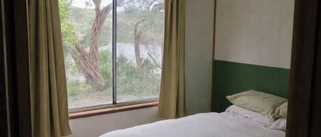 Een kamer met een bed, een raam met gordijnen en uitzicht op bomen.