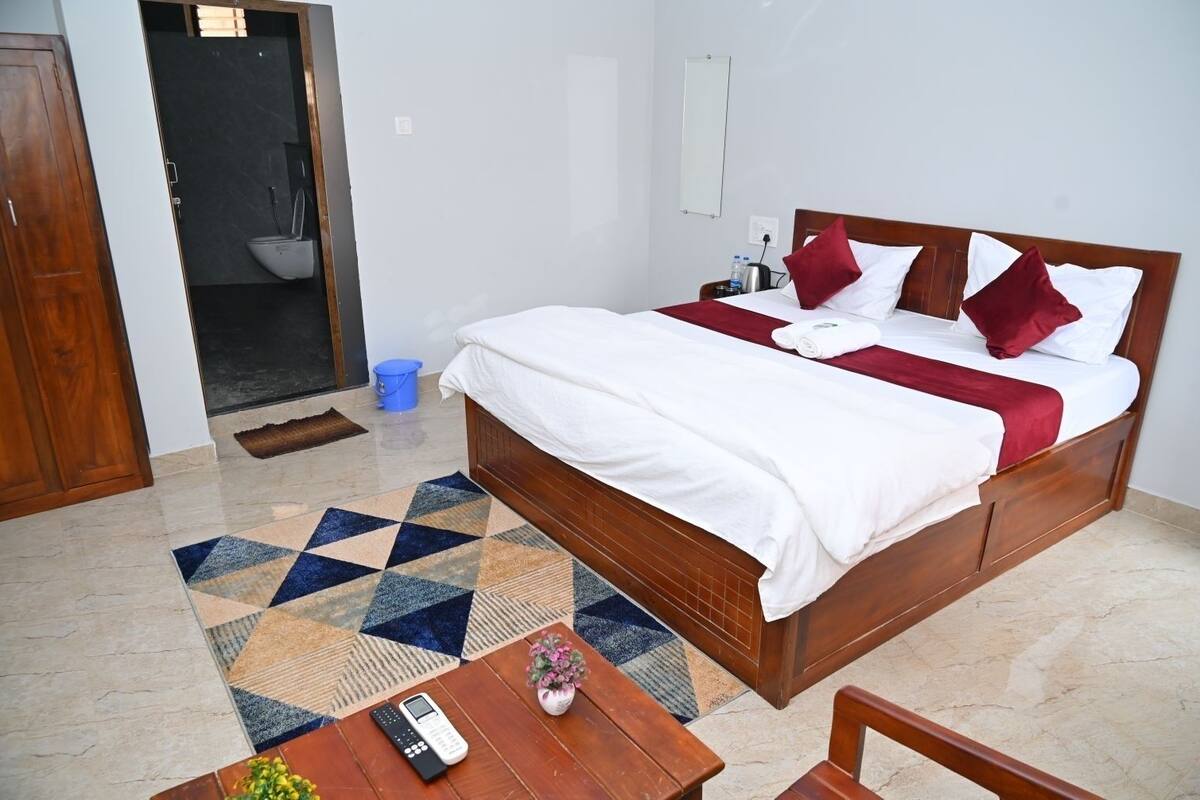 Ein Hotelzimmer mit einem Bett, einem kleinen Tisch mit Telefon, einem Sessel, einem blauen Eimer und einer Tür zu einem Badezimmer.