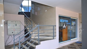 A reception area with a glass door, a staircase with metal railings, and a wall-mounted electrical panel. - AES Residency (Bhatkal)
