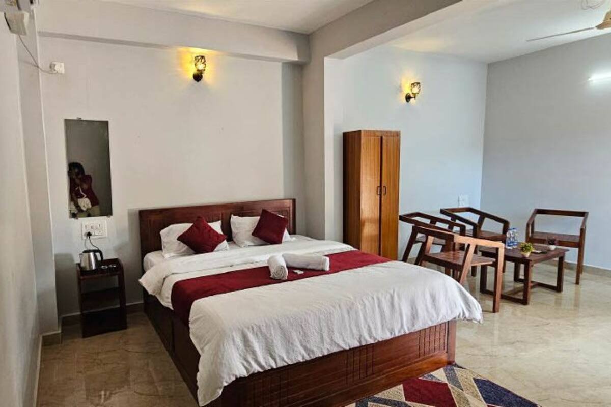 Ein Schlafzimmer mit Bett, Nachttisch, Lampe, Kleiderschrank und einer kleinen Sitzecke mit Stühlen und Tisch.