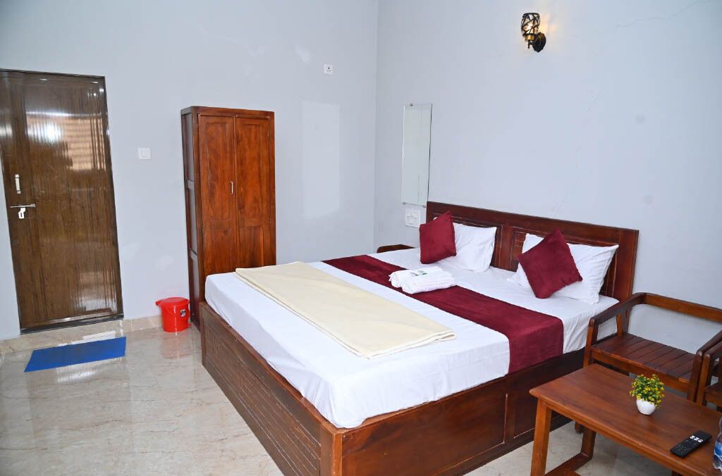 Een hotelkamer met een bed, een houten kledingkast, een nachtkastje met een plant, een spiegel en een rode emmer op de vloer.
