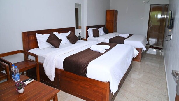 A hotel room with two beds, wooden furniture, a wardrobe, a desk with a keyboard, and a mirror. - AES Residency (Bhatkal)