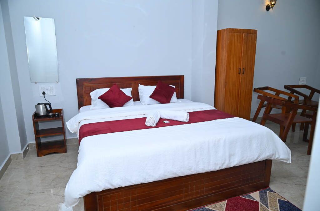 A neatly made bed with white and red bedding, a wooden headboard, a small bedside table with a kettle, and a wardrobe.