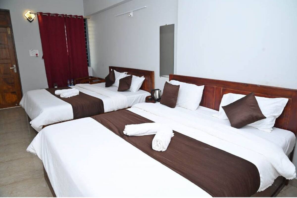 Ein Hotelzimmer mit drei Betten, jedes mit weißer und brauner Bettwäsche, einem Holz-Kopfteil und einem roten Vorhang.