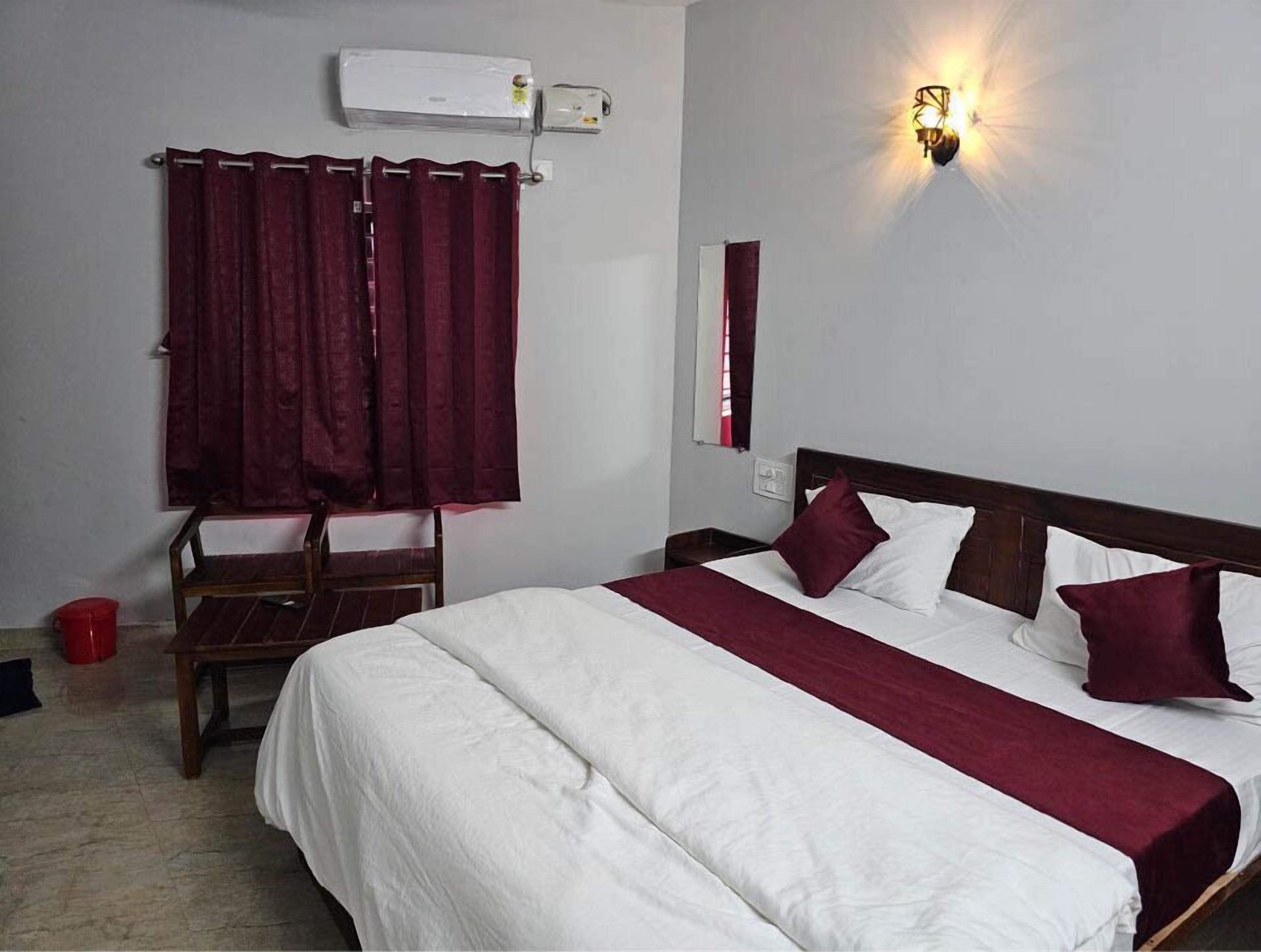 A hotel room with a bed, a chair, a red bucket, and an air conditioning unit.