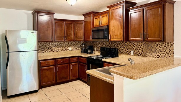 A kitchen with wooden cabinets, a stainless steel refrigerator, a microwave, and a stove. - Casa Granero, Waterfront 3BD/2BA w/ Private Yard! (Brownsville)