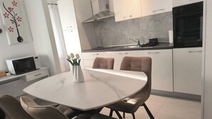 A modern kitchen with white cabinets, a black oven, and a marble dining table with four chairs. - Apartment Gea (Rovinj)