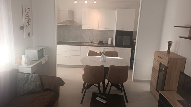 A modern kitchen with white cabinets, a dining table with chairs, and a TV stand with a flat-screen TV. - Apartment Gea (Rovinj)