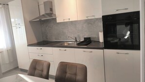 A modern kitchen with white cabinets, a stainless steel sink, a black oven, and two brown chairs at a table. - Apartment Gea (Rovinj)