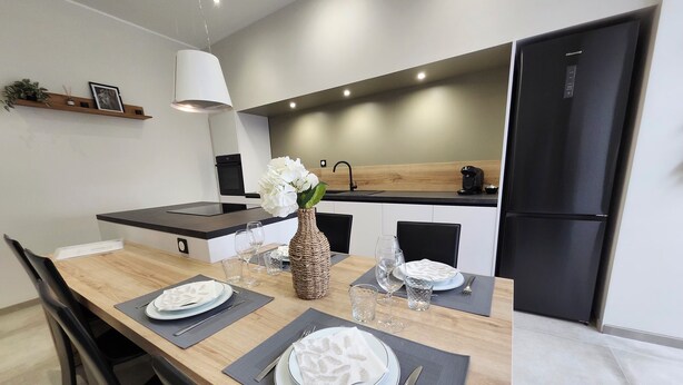 A modern kitchen with a dining area, including a wooden table set with plates, glasses, and a vase with flowers.