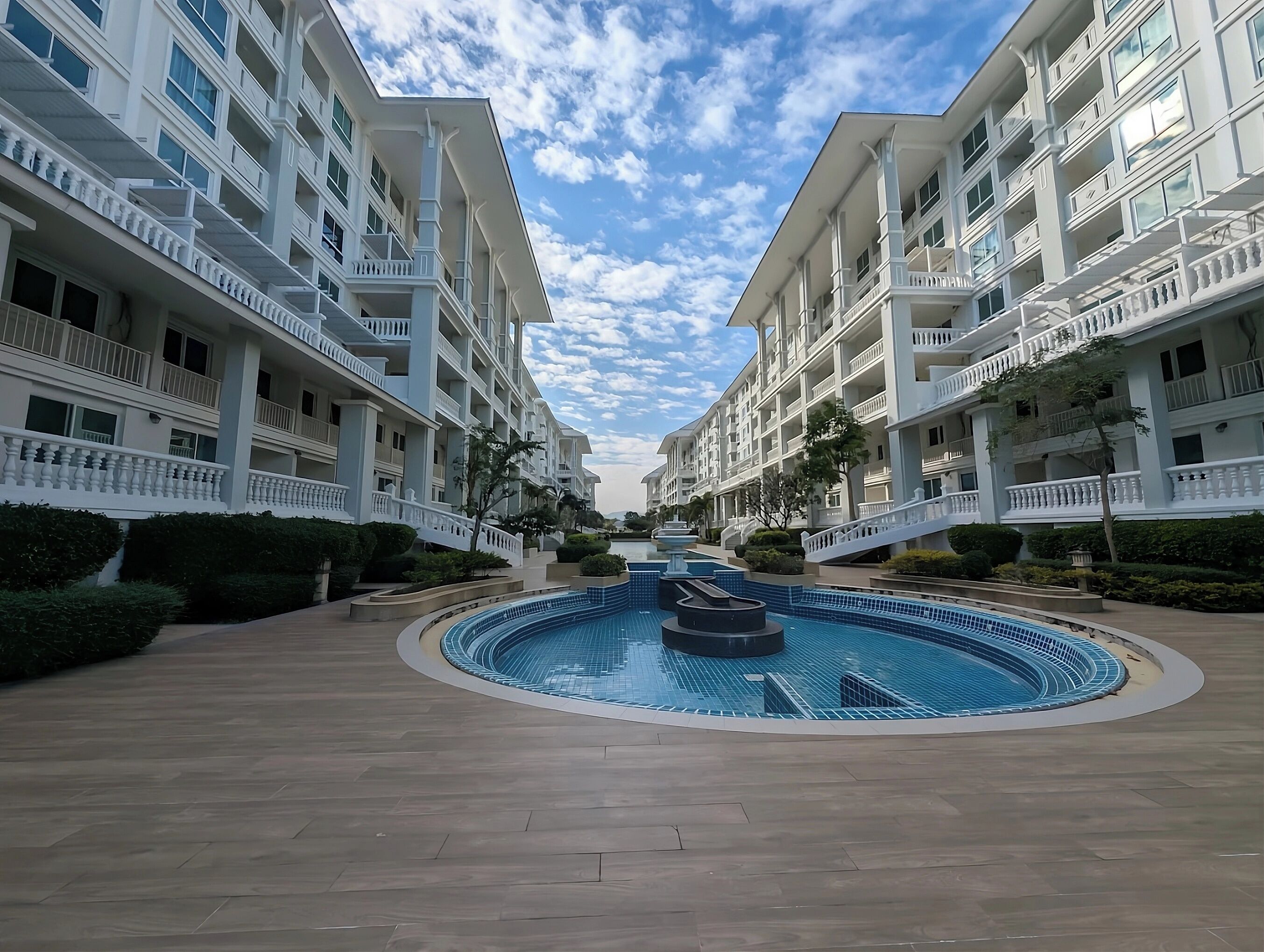 Un hotel con piscina central, varios balcones y cielo despejado.