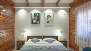 Un dormitorio con techo de madera, una cama doble con almohadas, dos mesitas de noche y una silla.