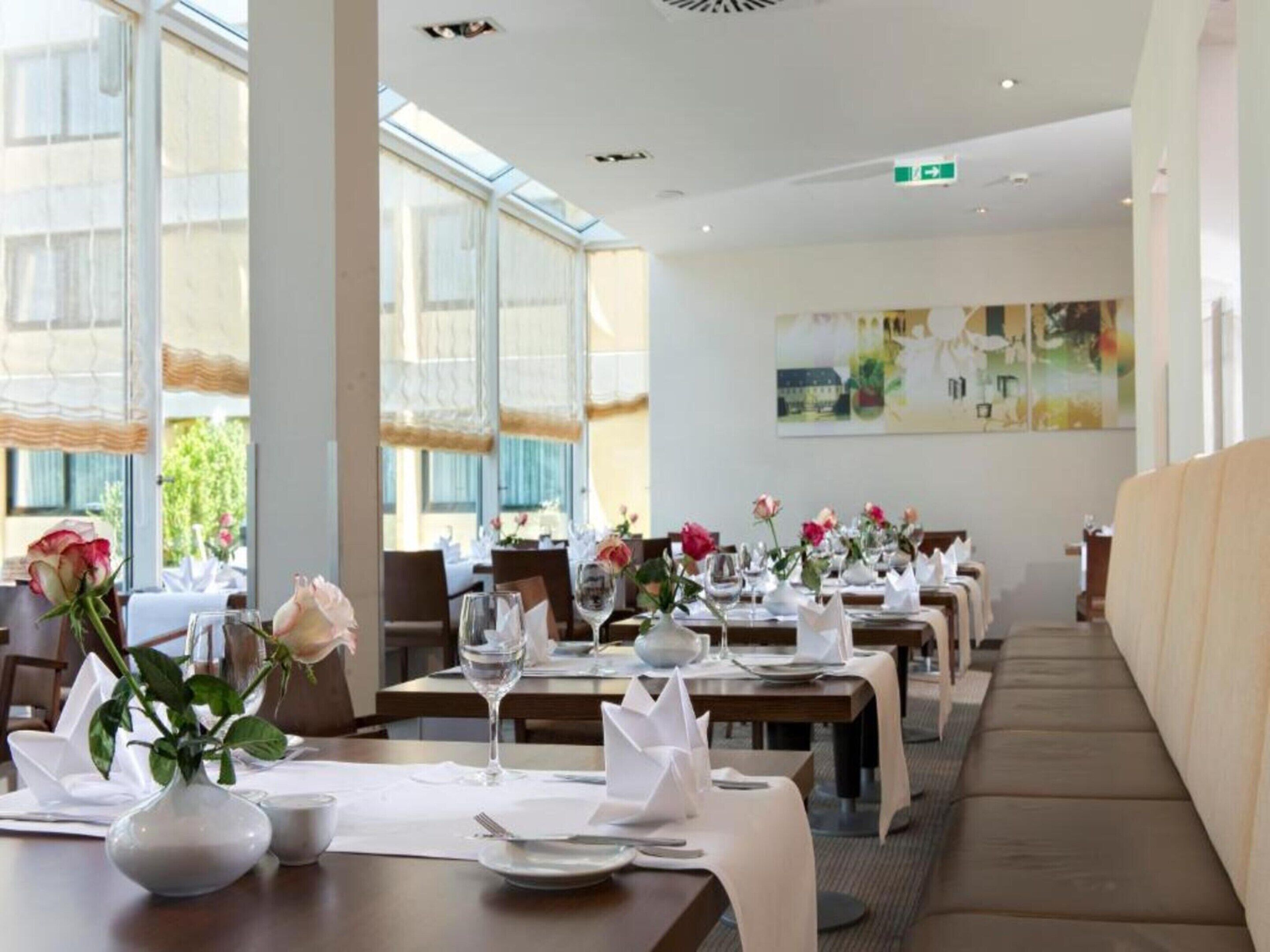 A restaurant with long tables, white tablecloths, and vases with flowers.