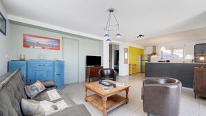 Ein Wohnzimmer mit einer Couch, einem Couchtisch, einem blauen Schrank, einem Fernseher und einem Küchenbereich im Hintergrund.