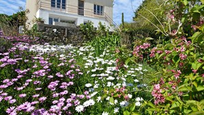 Ein zweigeschossiges Gebäude mit einem Balkon, umgeben von einem Garten mit verschiedenen Blumen.