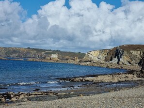 Un paysage côtier caractérisé par des falaises rocheuses, une plage de galets et un ciel bleu dégagé.