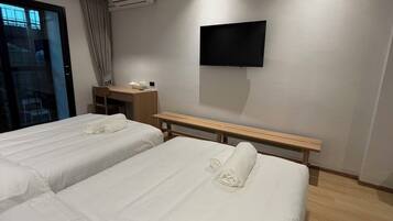 A hotel room with two beds, a desk, a flat-screen TV, and an air conditioning unit.