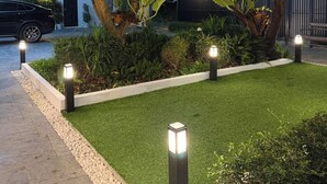 A well-maintained garden with a paved walkway, surrounded by trees and illuminated by ground lights. - 611 Hotel (Phetchaburi)