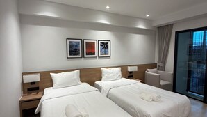 A hotel room with two beds, a nightstand, a chair, a window with a view, and three framed pictures on the wall. - 611 Hotel (Phetchaburi)