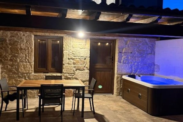 A stone exterior wall, a wooden door, a hot tub, and a table with chairs.