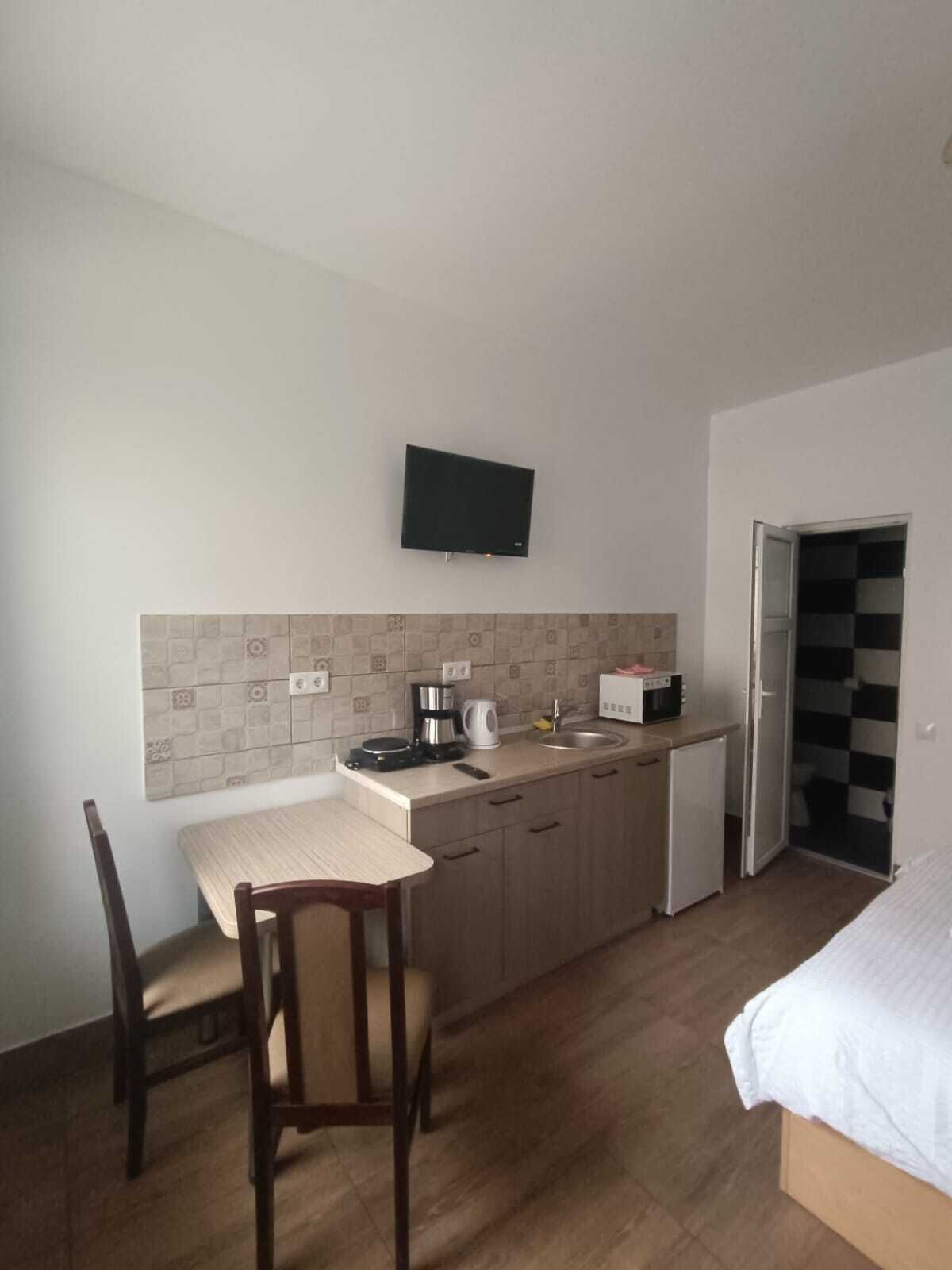 A compact kitchen with a dining table, chairs, a coffee maker, a microwave, and a TV mounted on the wall.