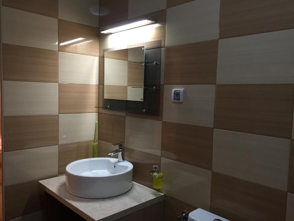 A bathroom with a white sink, mirror, and a light fixture above the mirror.
