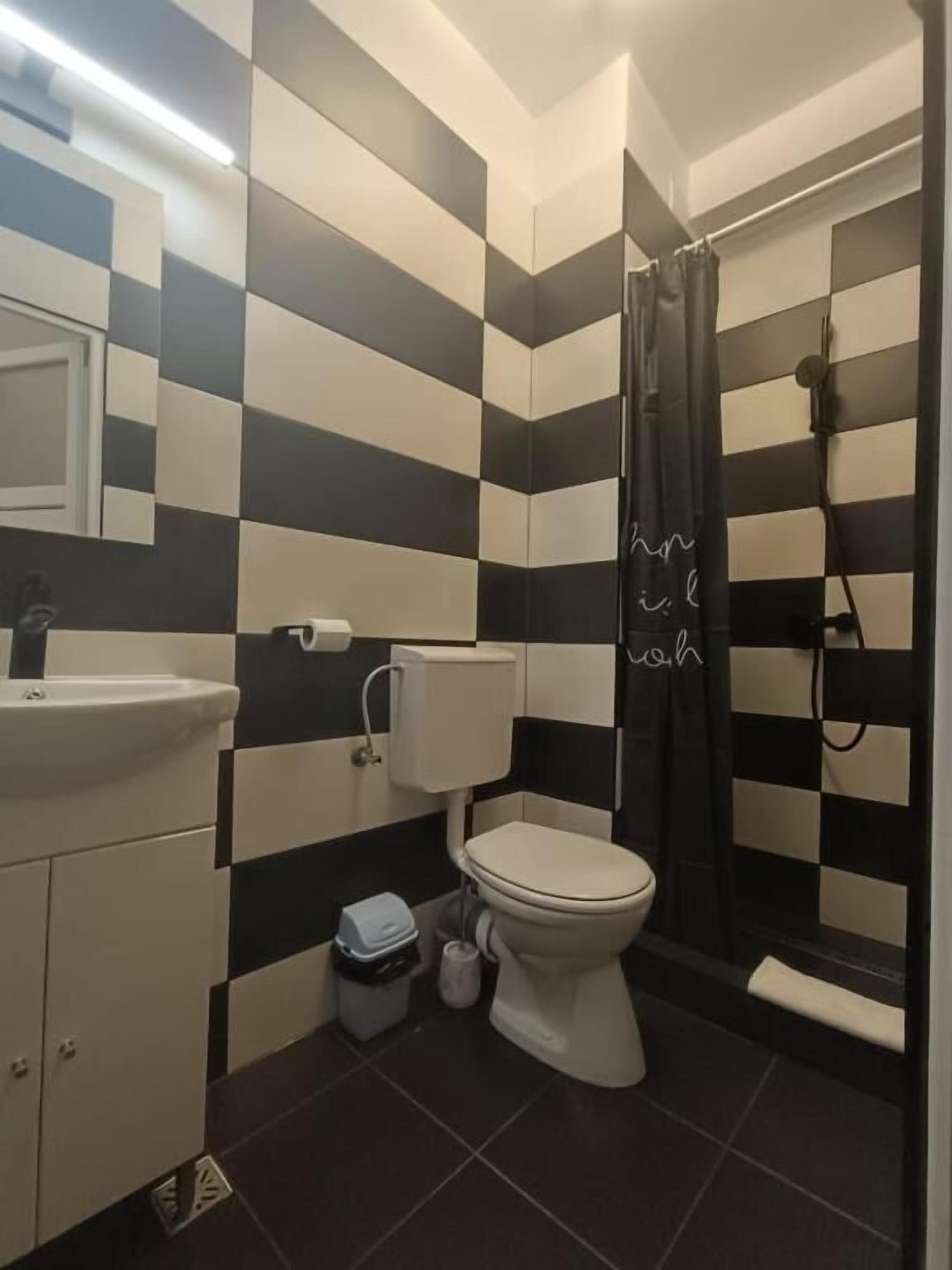 A bathroom with a black and white checkered wall pattern, a white toilet, a sink, and a shower area.