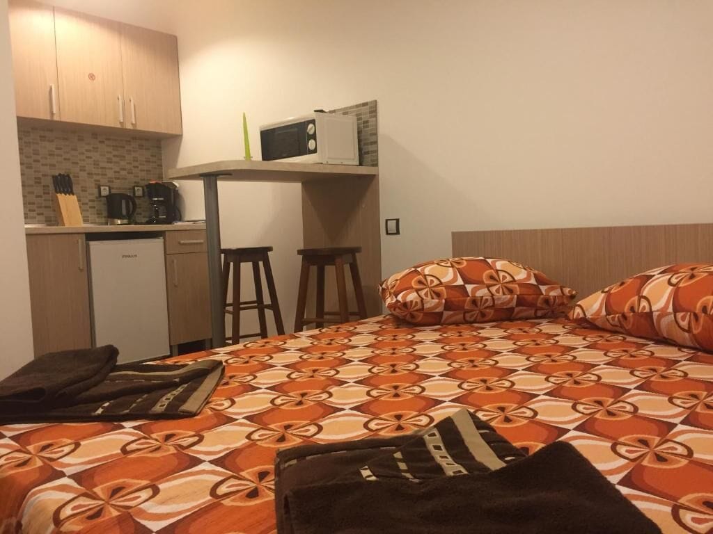 A compact room with a bed, a small kitchenette, and a single stool.