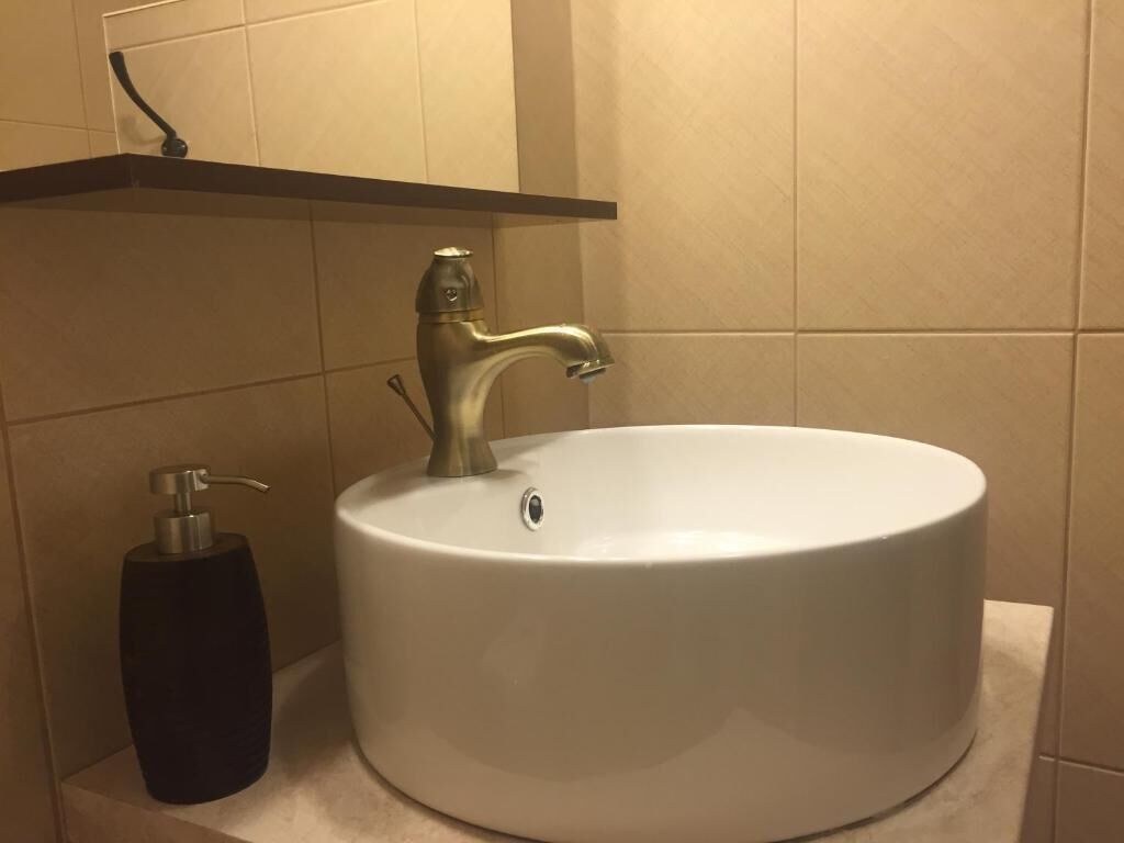 A bathroom with a round white sink, a faucet, and a black soap dispenser.