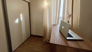 A room with a wooden desk, a laptop, a window with sheer curtains, and a plant.