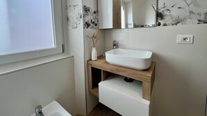 A modern bathroom with a white sink, wooden vanity, and a mirror above it.