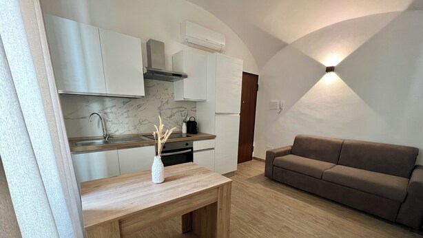 A modern kitchen with white cabinets, a marble backsplash, and a wooden dining table with a vase.