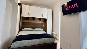 A bedroom with a bed, a wardrobe, a television mounted on the wall, and a small stool.