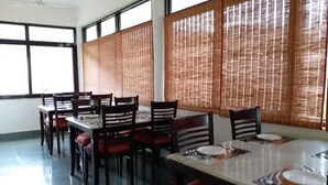 A dining area with tables and chairs, large windows, and a ceiling fan. - Home in the Hills Resort & Restaurant (Dehradun)