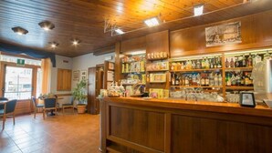 A bar area with wooden shelves stocked with bottles, a counter with a cash register, and a seating area with chairs and a table. - Hotel Appennino (Fiumalbo)
