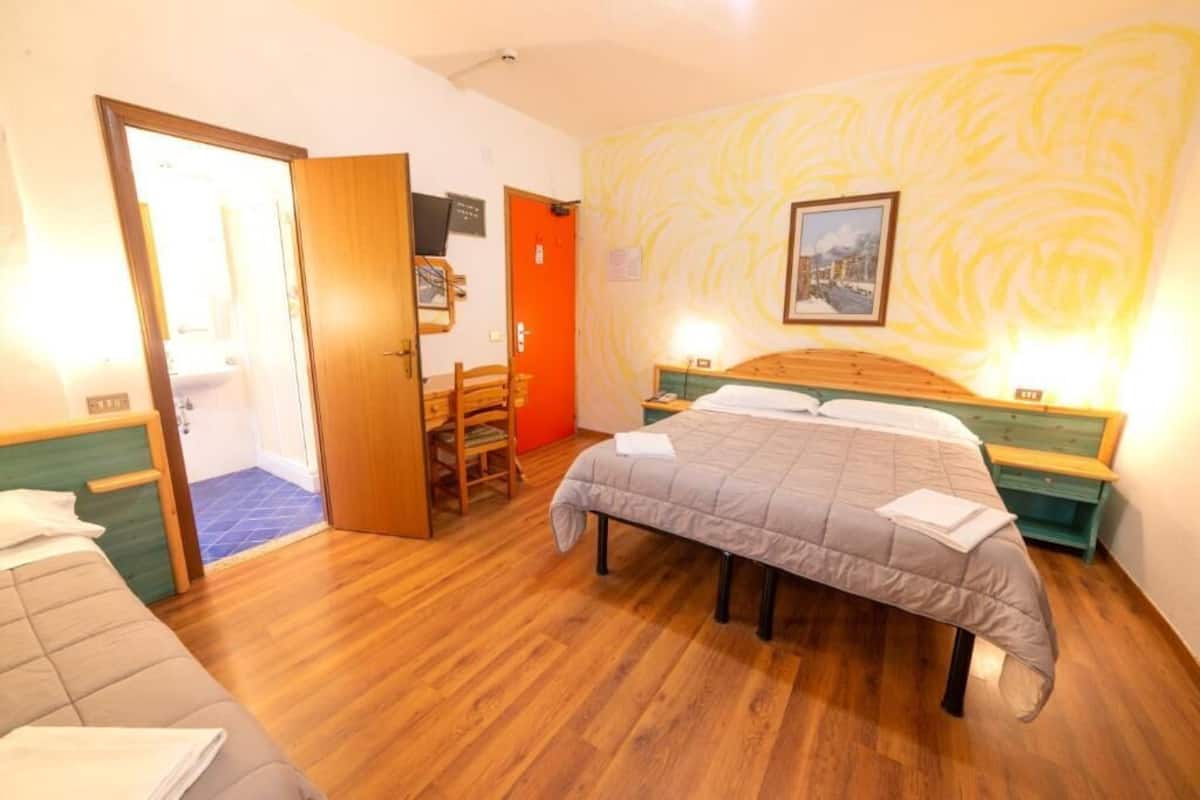 A bedroom with a bed, a wooden chair, a desk, and a door leading to a bathroom.