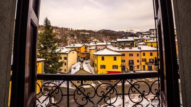 A balcony with a view of a town with yellow buildings and a mountain in the background. - Hotel Appennino (Fiumalbo)